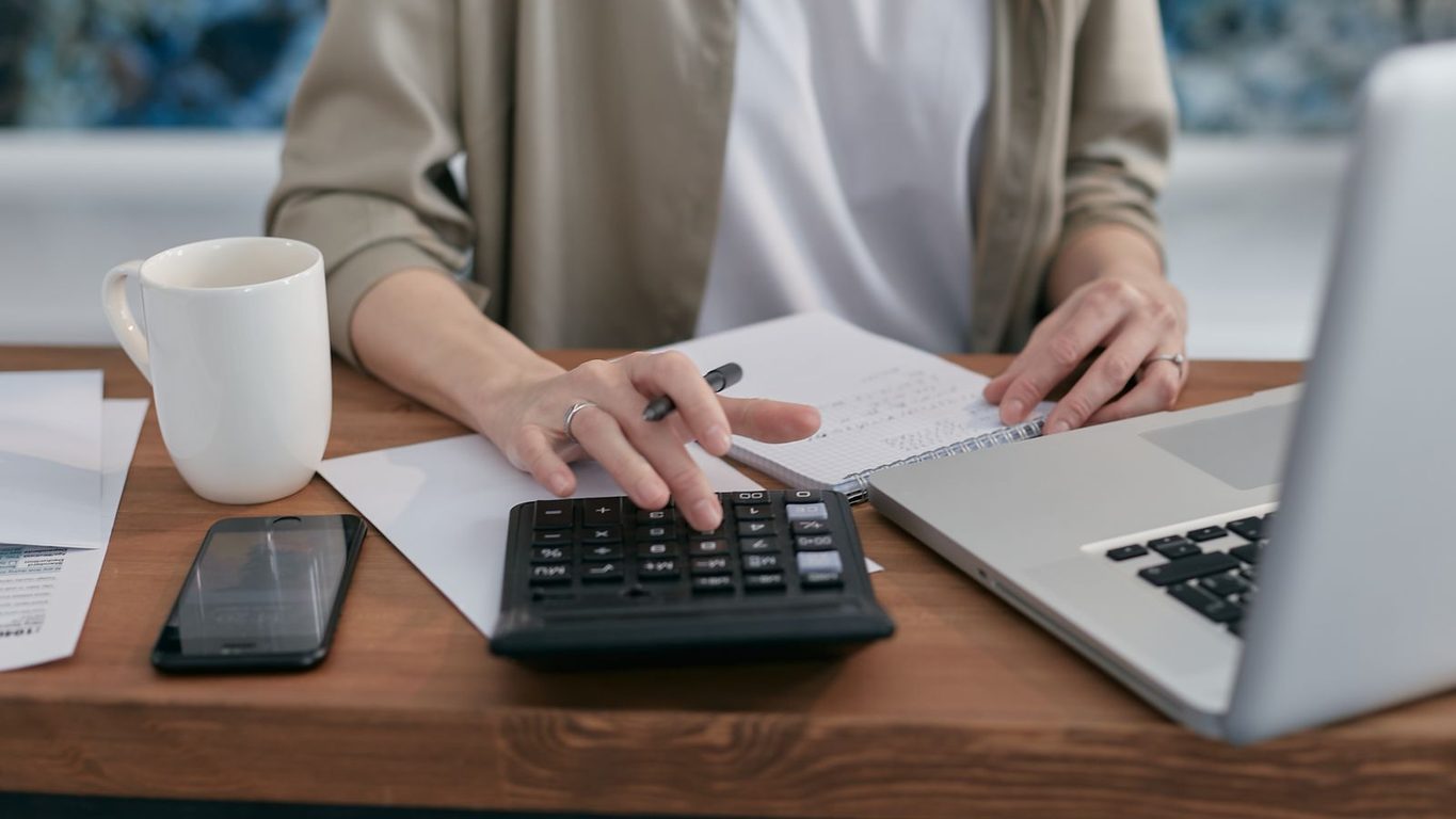 Persona haciendo cuentas con una calculadora y un celular sobre el escritorio