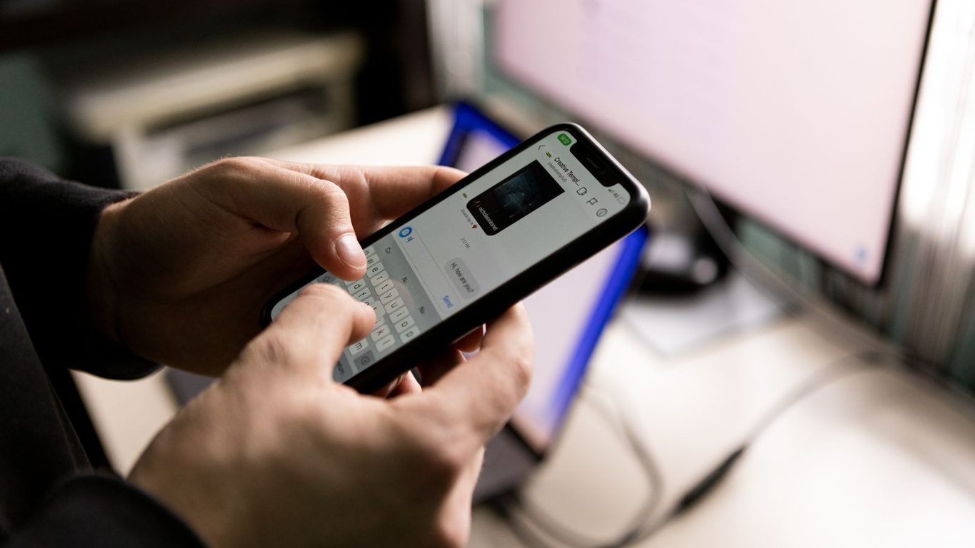 Manos sosteniendo un celular con mensajes sin responder frente a un computador