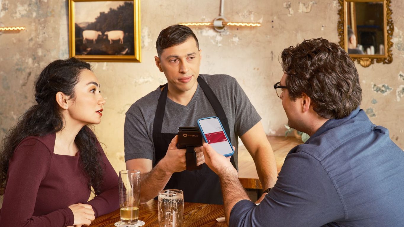 Mesero tomando el pedido con un celular mientras dos clientes miran la carta